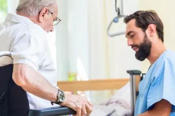 Photographie d'un aide soignant qui aide une personne âgée à s'asseoir.