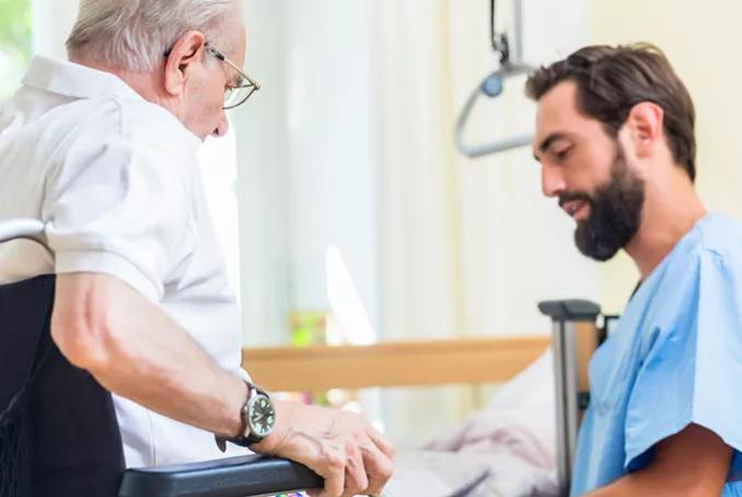 Photographie d'un aide soignant qui aide une personne âgée à s'asseoir.